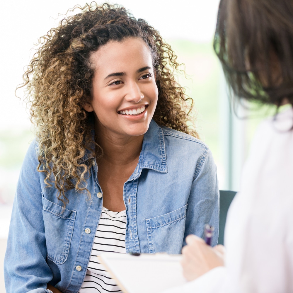 A doctor talks to a patient in her office. The patient is smiling.