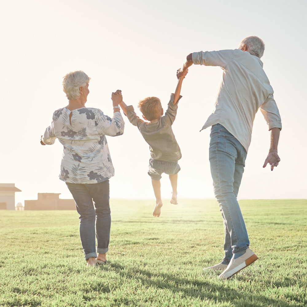 a child swings above the grass as they hold hands with their grandparents