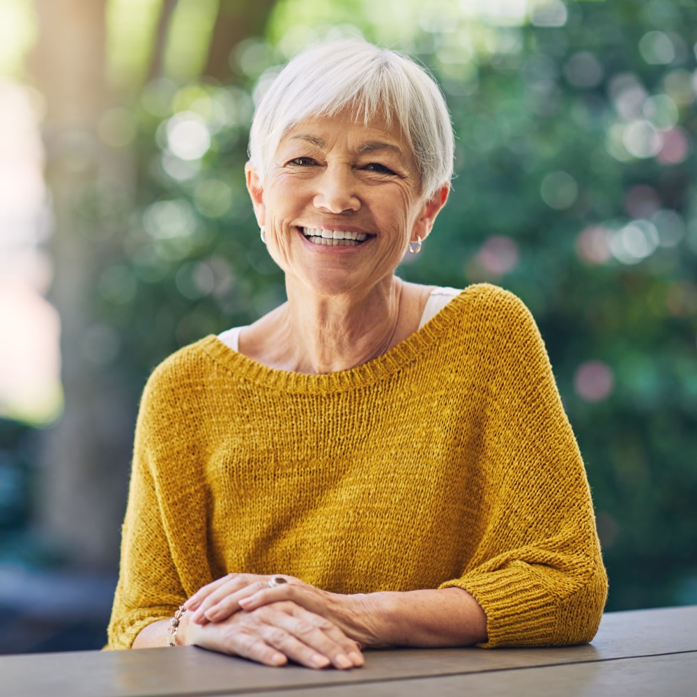 a senior women sits outside at a table and smiled