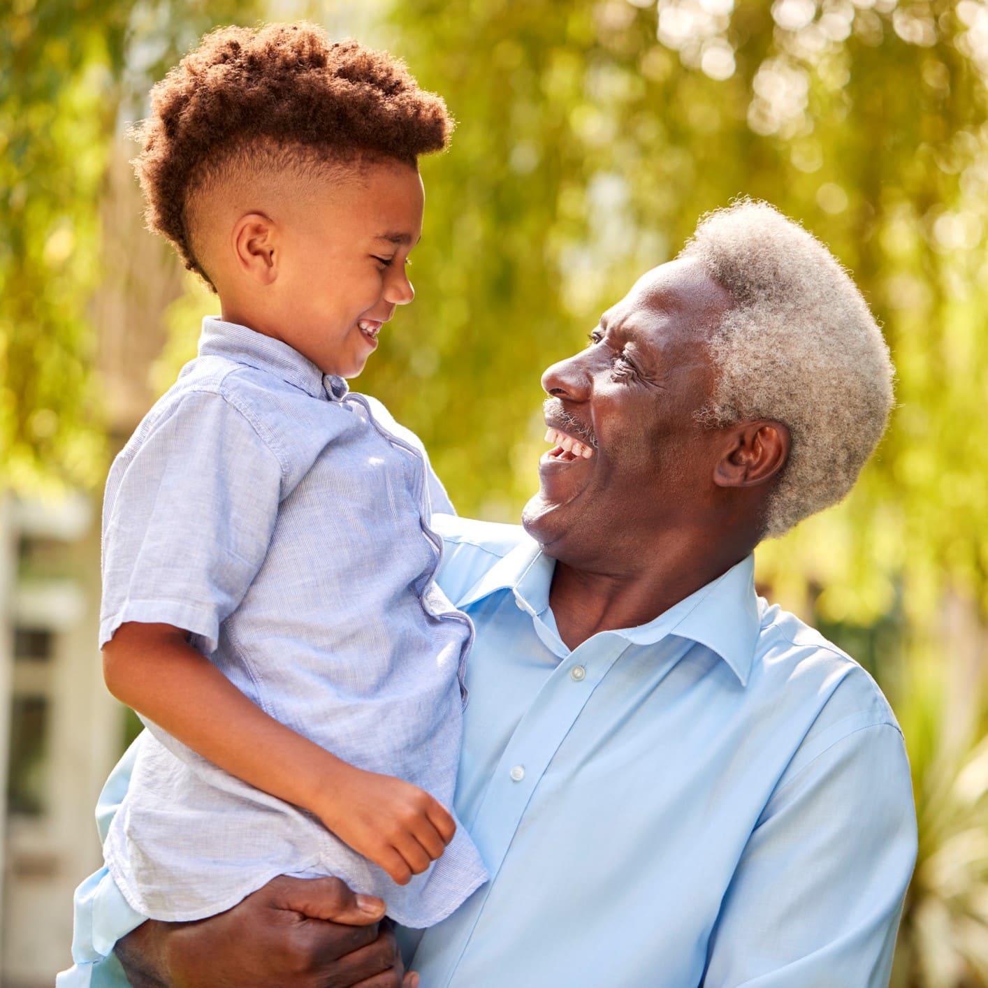 a grandfather holds his grandson outside with plants in the background