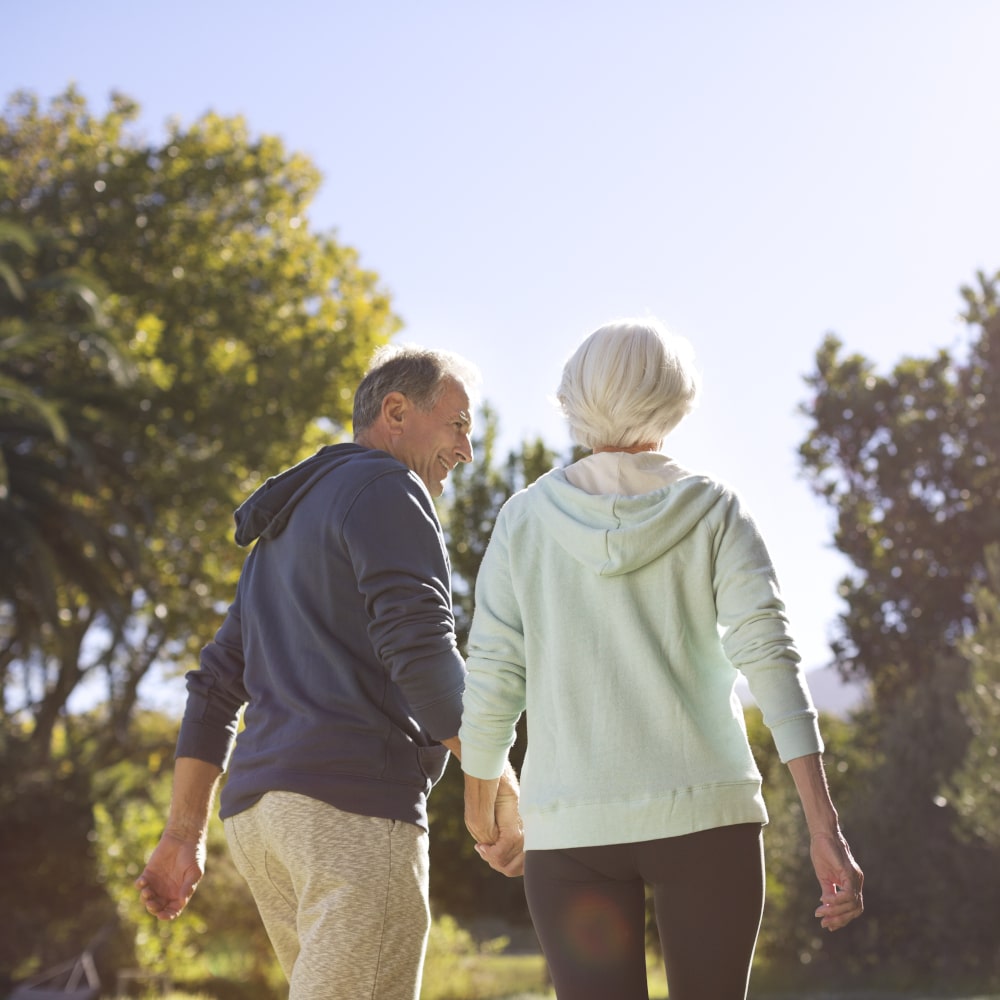 A senior couple holds hands and walks through a park